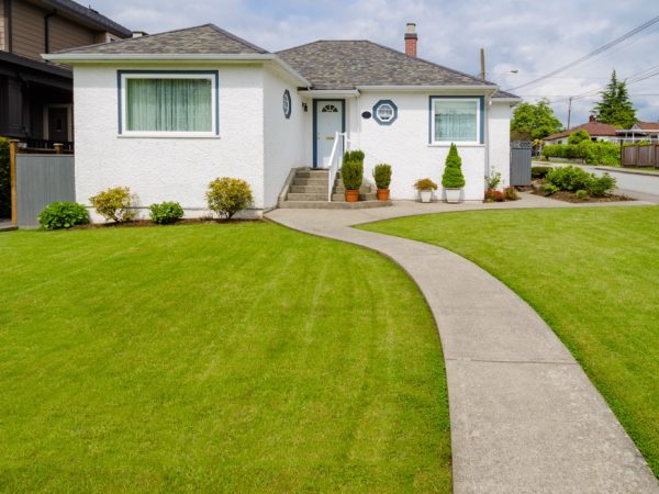 Main entrance of small residential house with concrete walkway over green lawn of front yard. Family house with doorsteps to the entrance