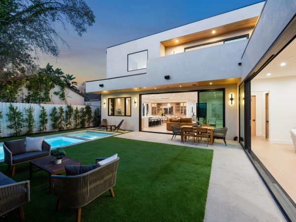 Modern luxury home with open living area, pool, and patio at dusk, featuring contemporary design and lush greenery.